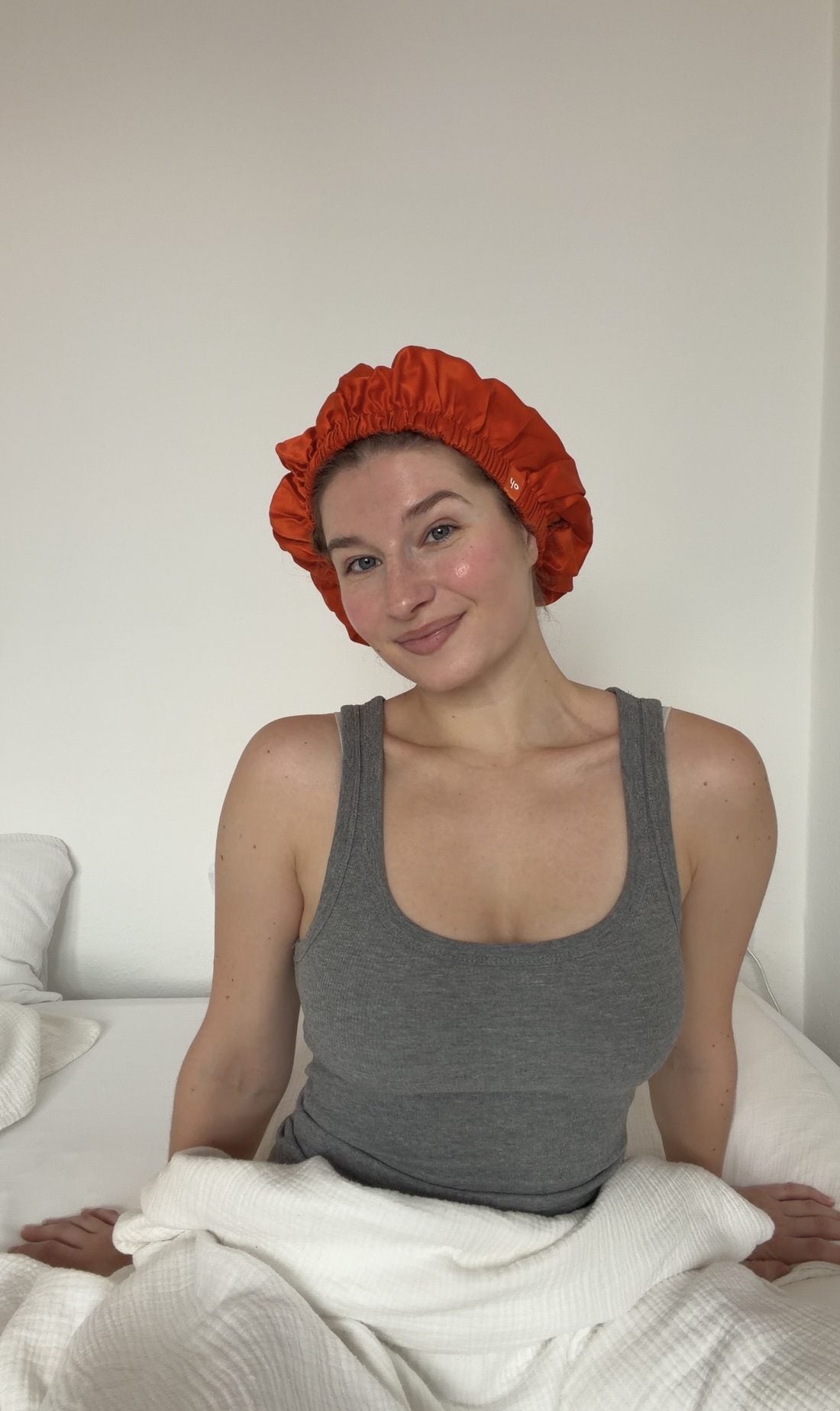 Frau sitzt morgens im Bett und trägt die orange ohsilk Seidenhaube